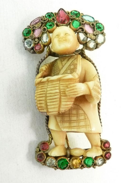 This famous Book piece by Hobe features a Asian Netsuke heavily carved figural with multi-color rhinestone accents. Her massive headdress is composed of round and marquise, unfoiled, open-back, rhinestones in shades of amethyst, pink and peridot.