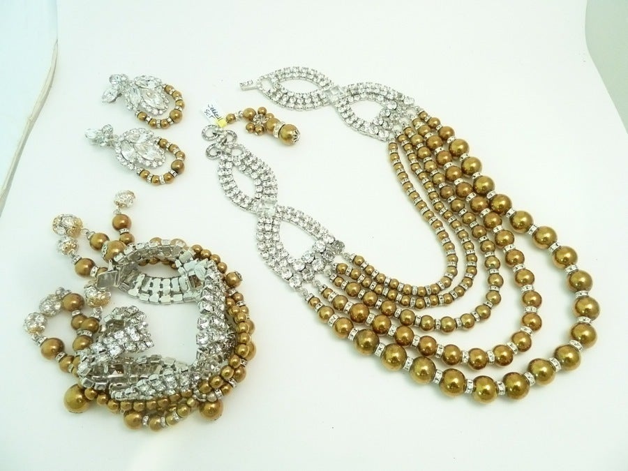 This signed One of a Kind Robert Sorrell set features gold-tone faux pearls with clear rhinestone accents in a silver-tone setting.  The necklace has an inside strand measurement of 18” with a hook closure; the clip earrings are 2 1/2” x 1 1/8” and