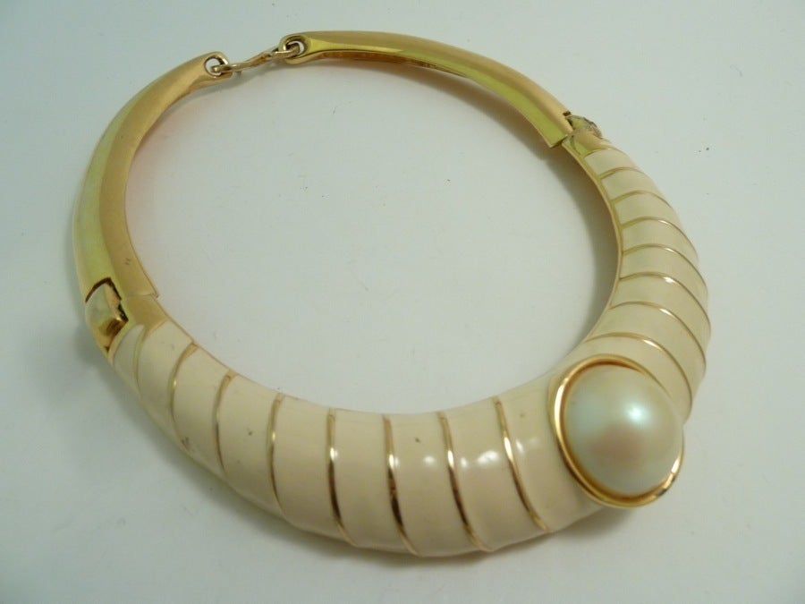 This early signed Alexis Kirk necklace features ivory color enameling with faux pearl accent in a gold-tone setting. It is a sturdy, beautifully made piece of jewelry.   In excellent condition, this necklace measures 18” x 1” with a hook closure and