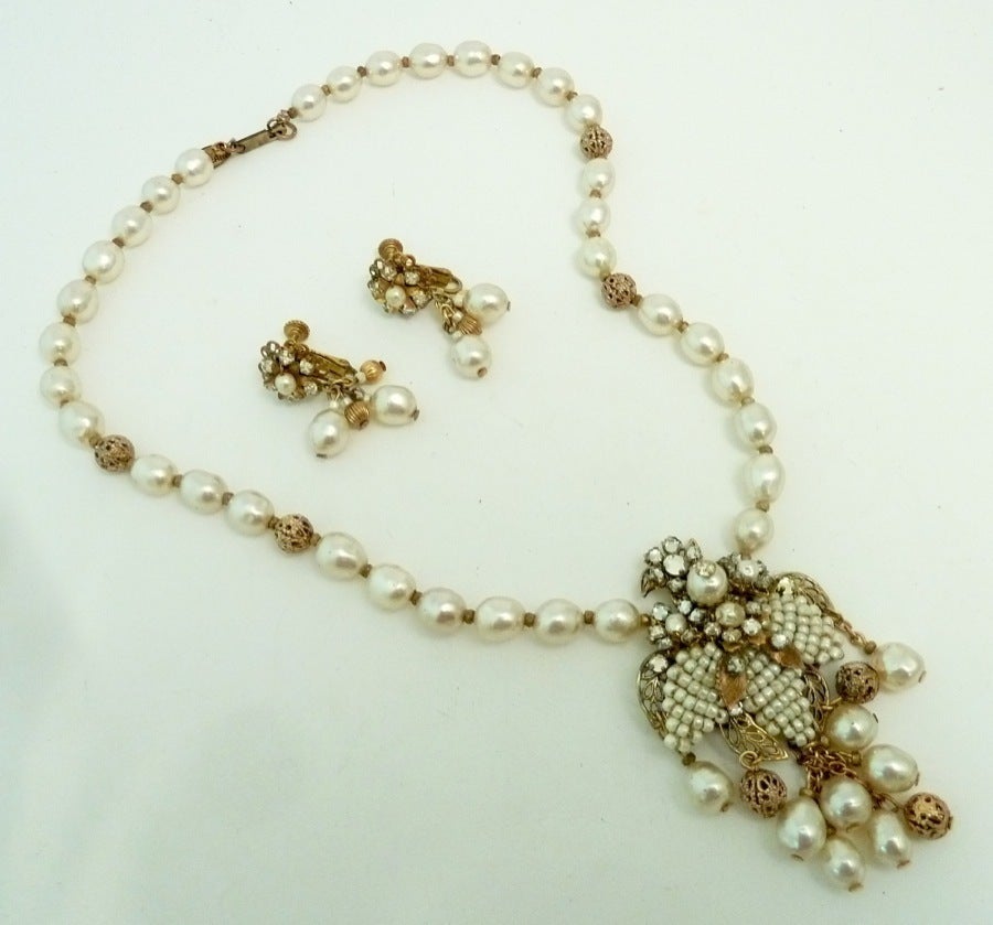 This vintage signed Miriam Haskell set features faux pearls and clear rhinestone accents in a gold-tone setting. The pendant measures 2 ¾” x 1 ½” wide and the necklace is 17” with a push/in closure; the clip earrings are 1 3/8” x 3/8”. We have