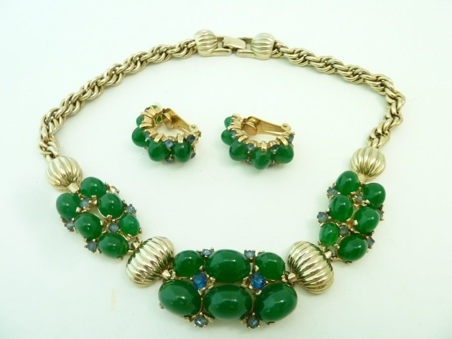 This well-known vintage Boucher set features cabochon cut green glass stones in a gold-tone setting.   The necklace measures 15 1/4” x 1” with a fold-over closure; the clip earrings are 1” x 7/16”.  In excellent condition, each earring bears the