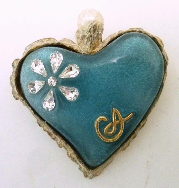 This vintage signed Christian LaCroix pin features a heart design with blue color glass and clear rhinestones and faux pearls in a gold-tone setting. In excellent condition, this pin measures 2” x 2” and is signed Christian LaCroix.