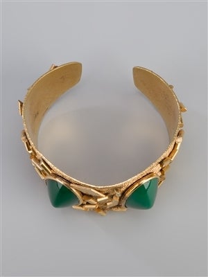 Gold-tone metal vintage cuff bracelet featuring a textured surface with geometric embellishments and green cabochons.

Material: metal, glass

Measurements:  width: 4.5 centimetres, circumference: 21 centimetres

Returns Policy: Final Sale -