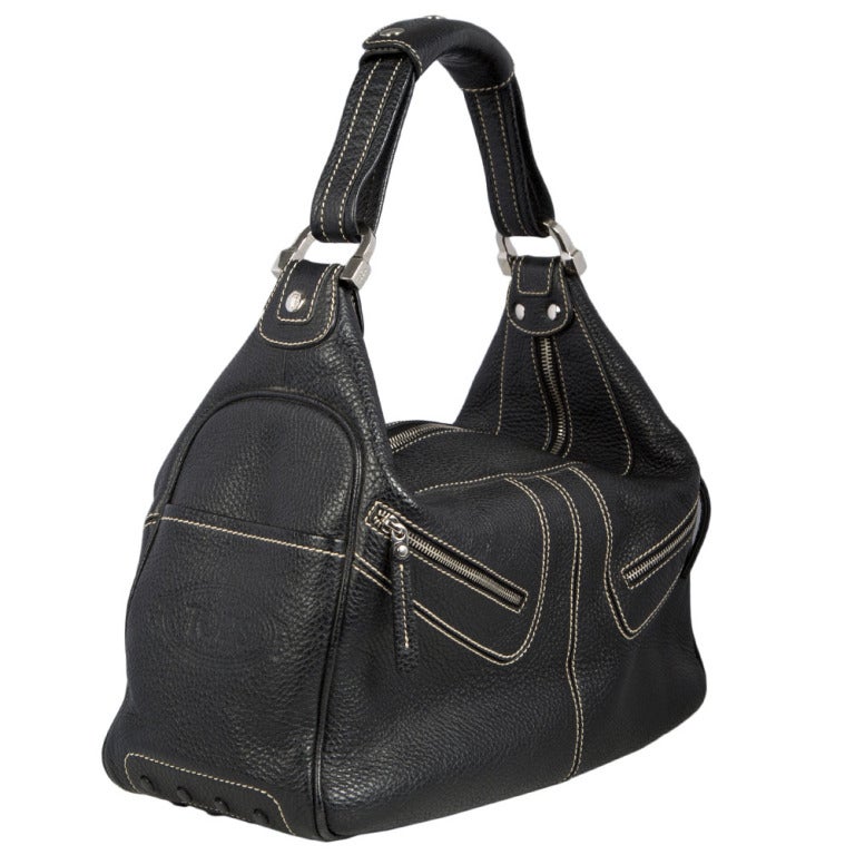 This black leather handbag by Tod's boasts two front zip pockets and is accented with gunmetal hardware. This piece features contrast stitching and zipped closure. There is also one open pocket on both sides and rubber studs on the bottom of this