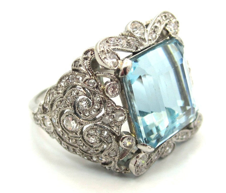 Impeccably handcrafted French Edwardian era ring composed of platinum with an intricate foliate motif pierced open work design.
Featuring a Square Step Cut Natural Aquamarine measuring 11.7-11.6 x 8.35 mm. Weighing an estimated 6.90 Carats.
