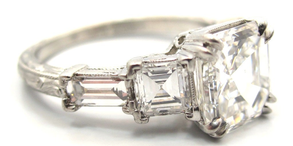 A fine example of the geometric shapes that exemplify the Art Deco era.
Handcrafted & composed of platinum with an intricate hand engraved filigree design on the shank & outer edges of the ring. Featuring a 1.90 Carat Asscher Cut diamond (Square