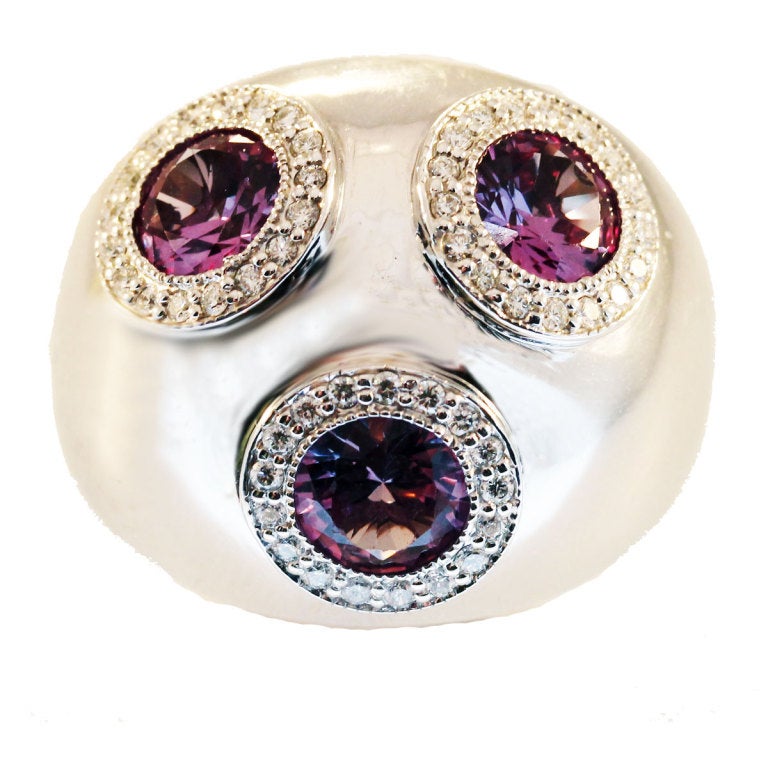 This striking womans three stoned 14k white gold ring is both elegant and fashionable. Featuring three large rare Alexandrite stones that are surrounded by beautiful pave set diamonds. The stunning Alexandrite stones change color from purple to