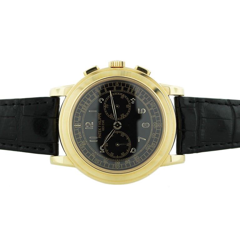 This Patek Philippe 18k yellow gold chronograph wristwatch, Ref. 5070J, has a black dial with Arabic numerals. The case has a display back showing the manual-wind movement. The watch is on a black leather strap that is adjustable. The crystal is