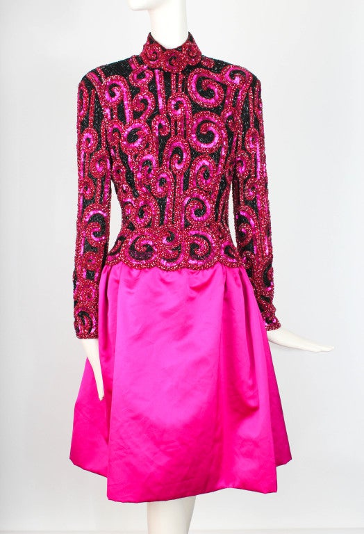 Dress presented by Bob Mackie Boutique in fuchsia with elaborate sequin and glass beading detail. This dress features a standing collar, scalloped waistline and zippered sleeves. The dress is fully lined in silk chiffon. 

Shoulder: 5.25