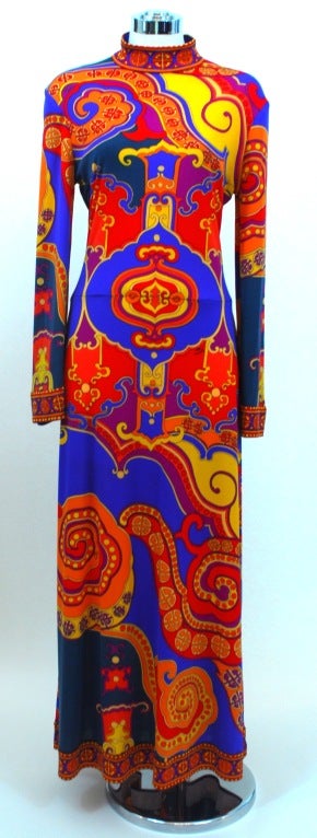 Dress presented by Leonard Fashion in jewel tones of red, orange, gold, blue and purple polyester. This dress features a mock neck, bell sleeves and geometric border along neck, sleeve and hem. Dress is unlined and has a back zip closure. Matching