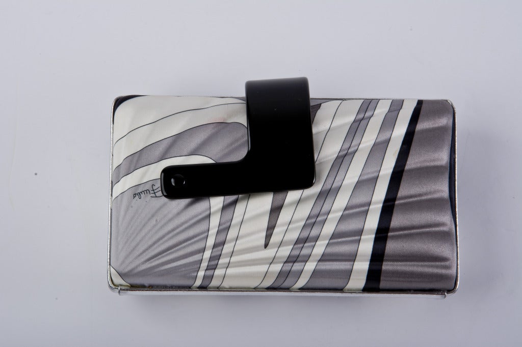 The 1960' s vintage clutch is covered in satin fabric with an iconic Pucci print in grey, black and white.  It has an interesting black plastic closure.  The inside is lined with silver tone hardware.  The outside has silver lame detailing.  Matches