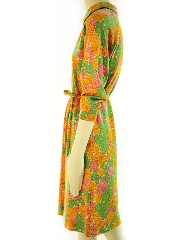 Dress presented by Goldworm in cream virgin wool knit with orange, green and pink flower print. This dress features a Peter Pan collar, raglan 3/4 sleeve with gathered cuff, thin self fabric belt and centered zipper back closure. Unlined.  