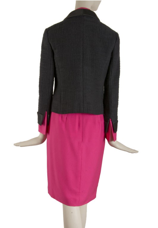 New with tags, this Chanel three piece suit is presented in black and magenta pink.  The The sleeveless blouse is magenta pink silk with a button front closure.  The buttons are gold tone with pearl and a green bead.  The black jacket is cotton with