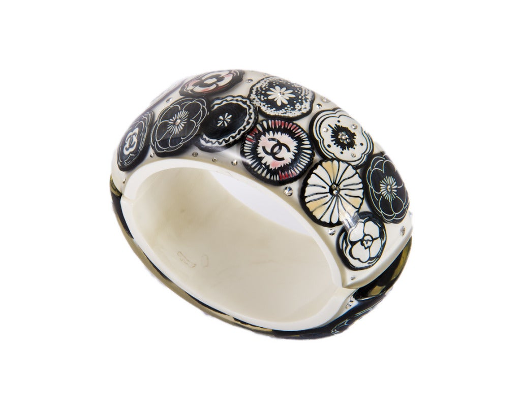 This bracelet is white with black camellia flowers and CC logos.  It also has crystals scattered throughout.  Some of the flowers have hints of color-see photos.  This bracelet is hinged with a magnetic closure.  It originally retailed for $2750.00.