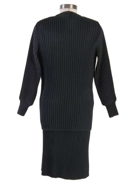 This iconic 1980’s 3-piece cardigan sweater set & skirt ensemble by American designer Mary McFadden presented in black ribbed knit wool features elongated cardigan with jewel neckline and matching long sleeve sweater with boat neckline, wide banded
