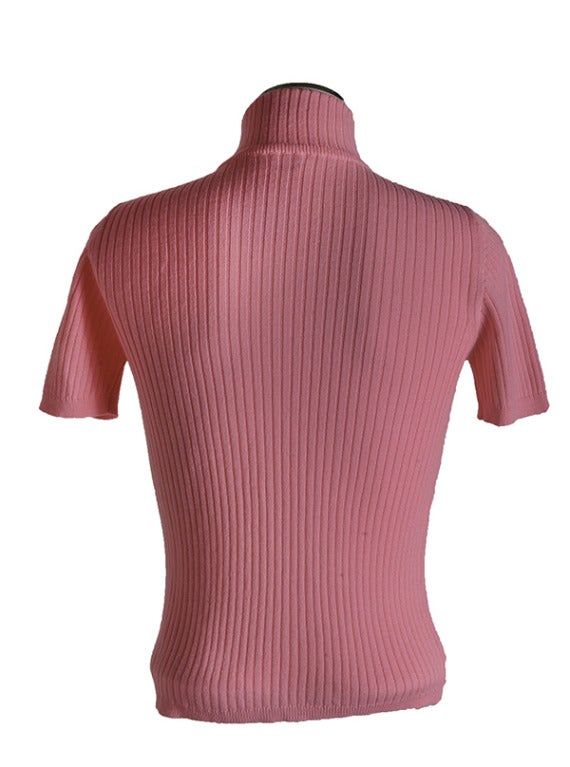 This new, never worn,  sweater is presented in bright pink ribbed knit/acrylic blend.  It features a mock turtleneck and short sleeves.  It also has a Courreges logo on the center chest area and banded sleeves and waist.