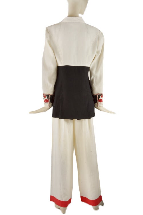 This vintage pants suit is presented in linen. The jacket is lined with silk.  It is white with black and red trim and features beaded wrists and pockets.  The jacket is double breasted with pink, red and gold tone buttons and shoulder pads.  The