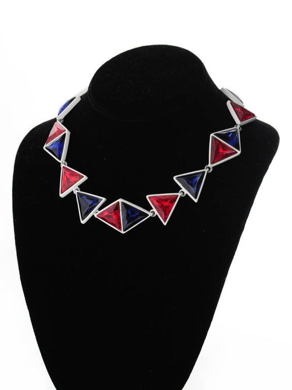 Presented here is a unique vintage necklace from renowned designed Kenneth J. Lane. The necklace is composed of a white metal necklace with red and blue triangular rhinestones encrusted into the metal. The necklace has a metal fold-over clasp