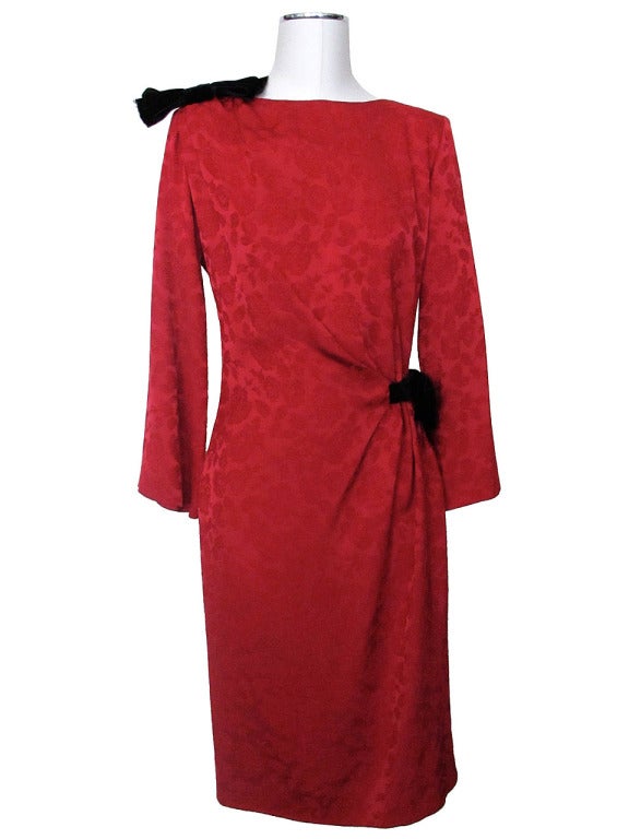 Luxurious red silk brocade dress with subtle rose motif and two black velvet bows. Rounded neckline with black velvet bow on right shoulder. Silk fabric drapes to left side of waist and is gathered by a single black velvet bow. Hidden side zipper