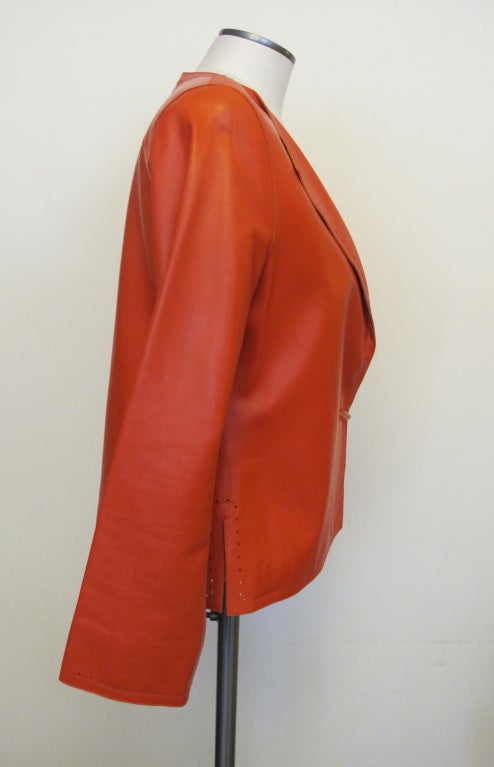 Dazzle in this buttery soft leather jacket in striking rich orange. Pointed lapels with single tangerine toned lucite button closure; miniature cut-out triangles trim the whole jacket from lapel, collar, cuffs to entire perimeter; 4