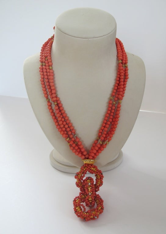 This vintage William de Lillo Necklace has four strands of faux coral beads knotted and gathered to lead into a pendant comprised of three linked gold tone rings, caged in by smaller faux coral bead strands accented with rhinestones. Necklace