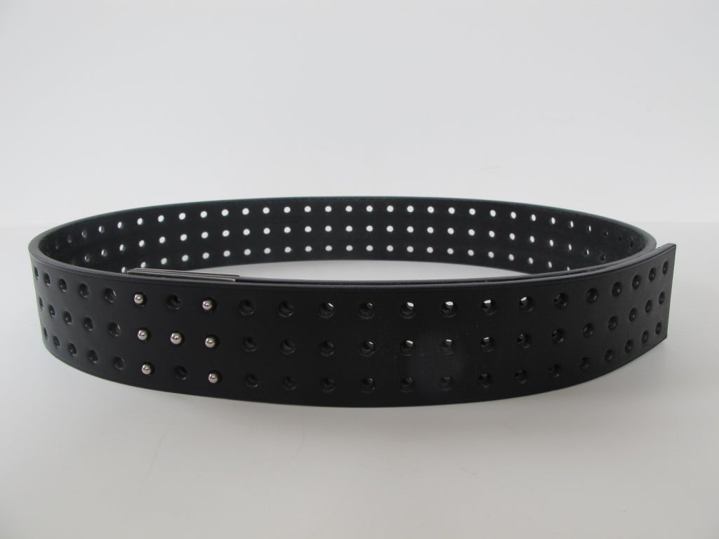 Adjustable leather belt due to motif of 3 rows of hole inserts. When belt is fastened, hole design forms the letter 