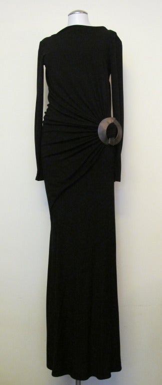 Long black stretch gown with large round detachable buckle gathered at the hip with low asymmetrical black and long sleeves. Length of the gown is 64 inches and the sleeve length is 25 inches.