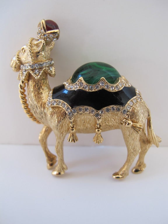 Majestic signed Ciner figural camel. The camel has a black enamel saddle with a green cabochon center stone and trimmed with pave set clear rhinestones and moveable tassels. Camel carries on his head a pave crown set with a red cabochon stone and