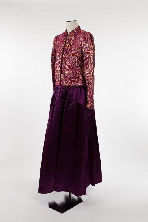 Regal open jacket with full, long party skirt. the gold silk brocade jacket with a festival motif in eggplant and deep red; the collar of a quilted band that extends down the opening and around the jacket hem; long sleeves terminating in quilted