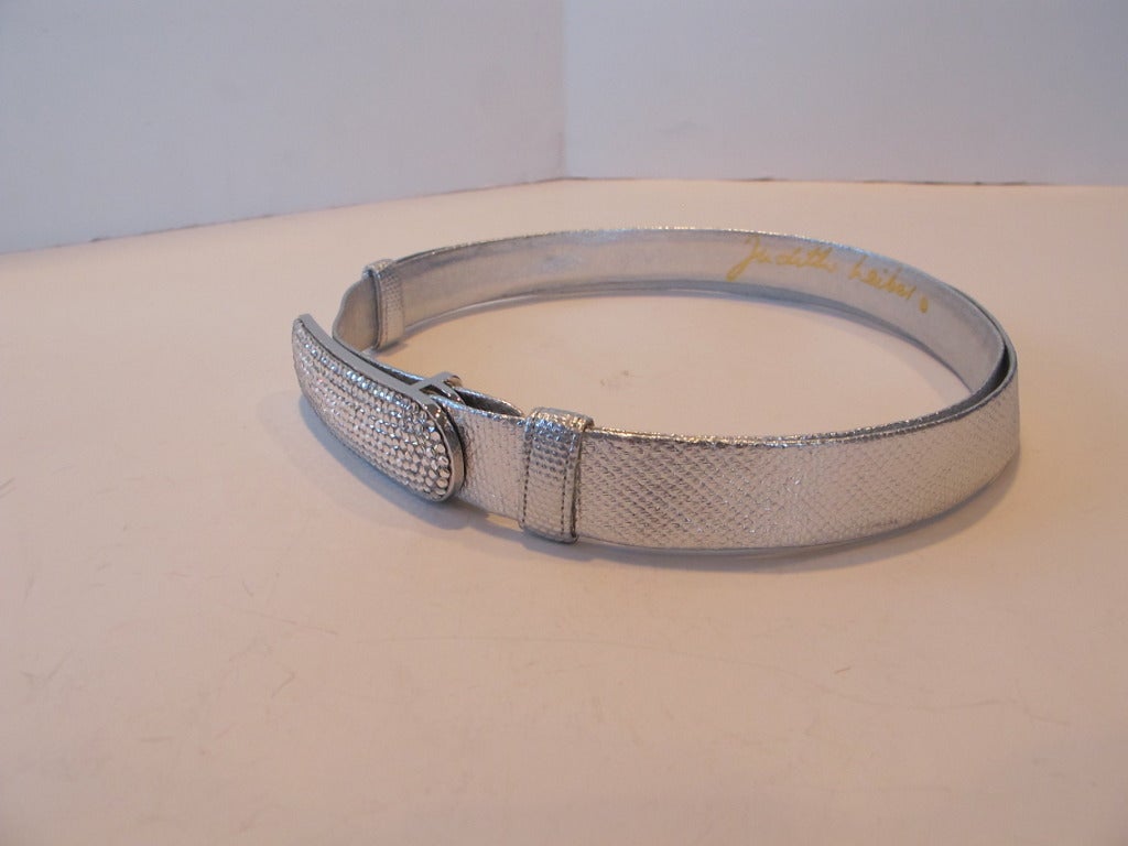 Buttery soft silver leather belt in lizard design. Belt is adjustable and accented by Iconic Judith Lieber rhinestone buckle measuring 3.5 inches long by 1 inch wide. Belt is 1 inch wide and is adjustable. The belt measures 43.25 inches total
