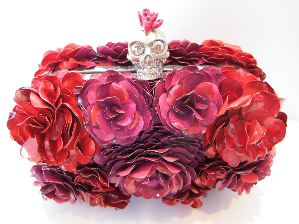 Luxurious Alexander McQueen flowered encrusted skull clutch. The flowers are red, magenta and fuchsia. Some of the flowers features heart shaped flower petals. The iconic skull enhanced by a mohawk (missing 2 beads) opens the bag. The skull is