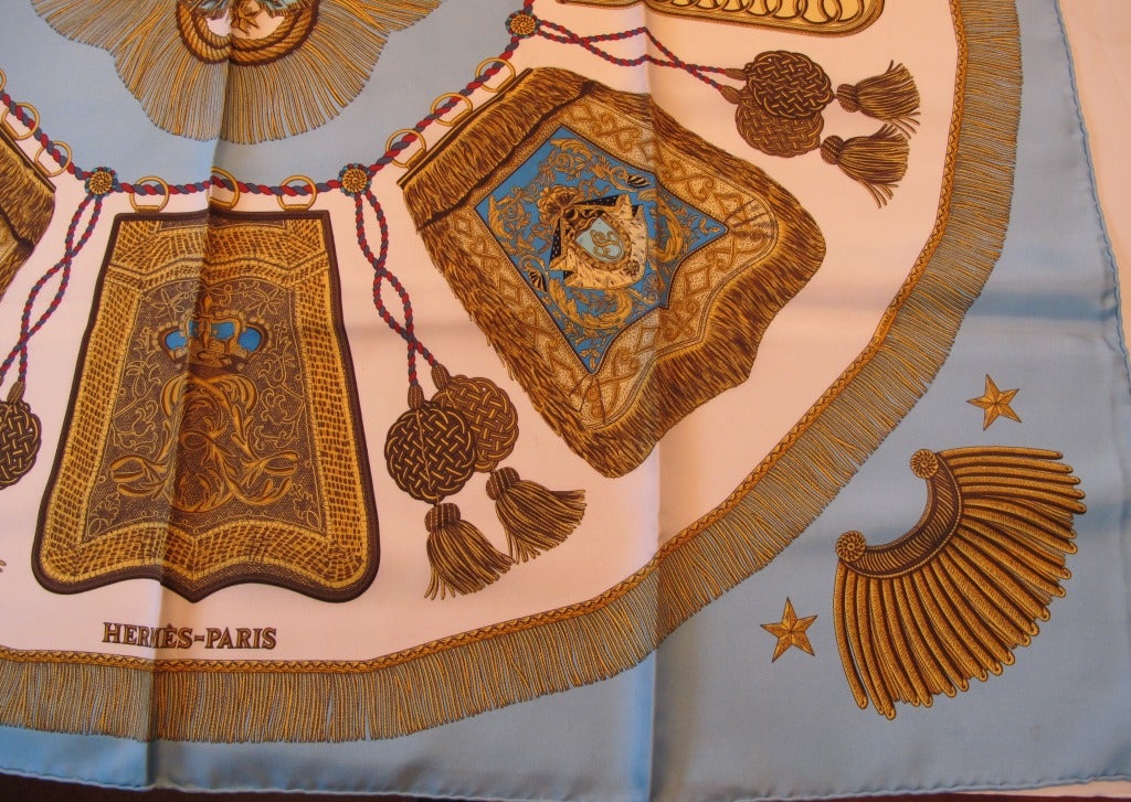 Hermes Poste et Cavalerie silk scarf is  by Joachim Metz. The background is French blue and features the designs of golden shoulder epaulets, emblems stars and tassels. Hand stitched and hand rolled hem.