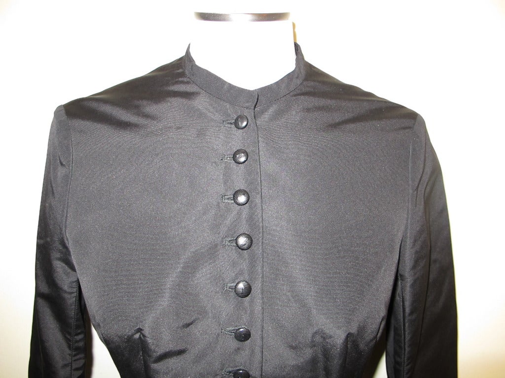 Iconic Black silk taffeta Alexander McQueen fitted to the waist jacket with 12 buttons (1 button missing). Double pleat in back. Cuffs are pleated; width measures 5 inches in the middle of the cuff, there is a 3/4 inch leather strip. Collar is 1/2