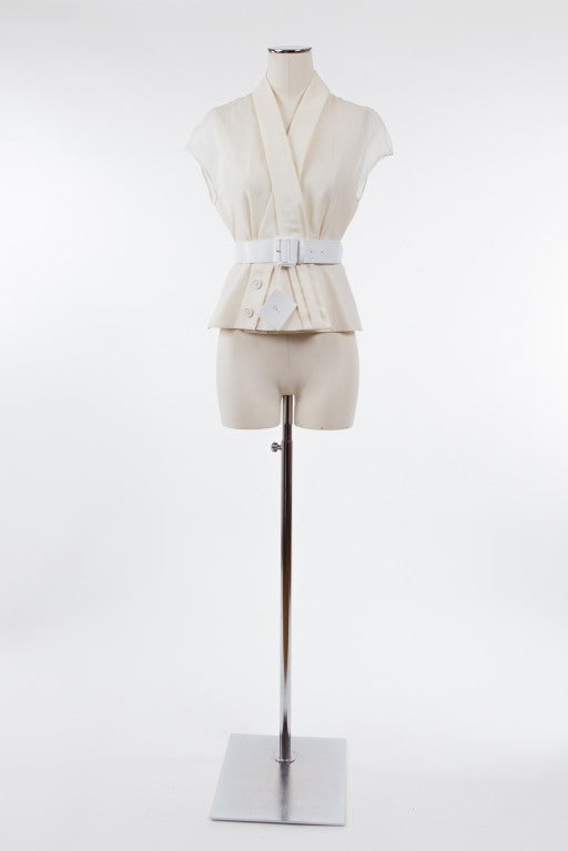 Super chic cream-colored sleeveless wool and silk blouse. Flat collar forms a V and crosses over and fastens with a hidden snap. One side terminating in three  Dior stamped buttons, the other side terminating in three pleats; fabric has weight but