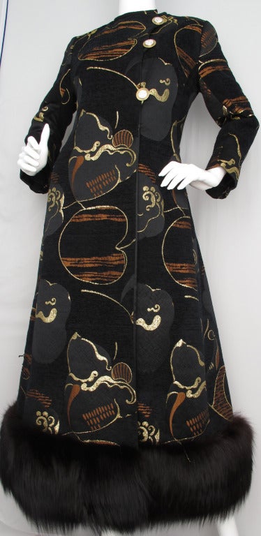This killer 1970s coat by designer Bill Blass features a graphic pattern of alternating brown and black chenille embroidery with black duchess satin embroidered with gold metallic thread in an abstract design. Details include fur trim at the hem,