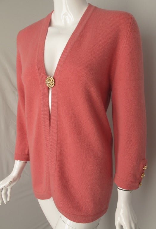 A Chanel cardigan in rose pink made from luxurious Scottish 100% cashmere. Fastening at the front by means of a singular rhinestone-encrusted button - the rhinestone button motif continues at each cuff with with three floral rhinestone buttons each.