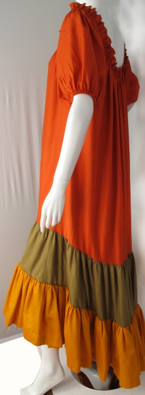 A late 70s/early 80's Yves Saint Laurent floor length red-orange peasant dress made from 100% polished cotton with a color block ruffle hem in a classic YSL palette of burnt orange, red-orange and olive green. The top of the dress is a scoop neck