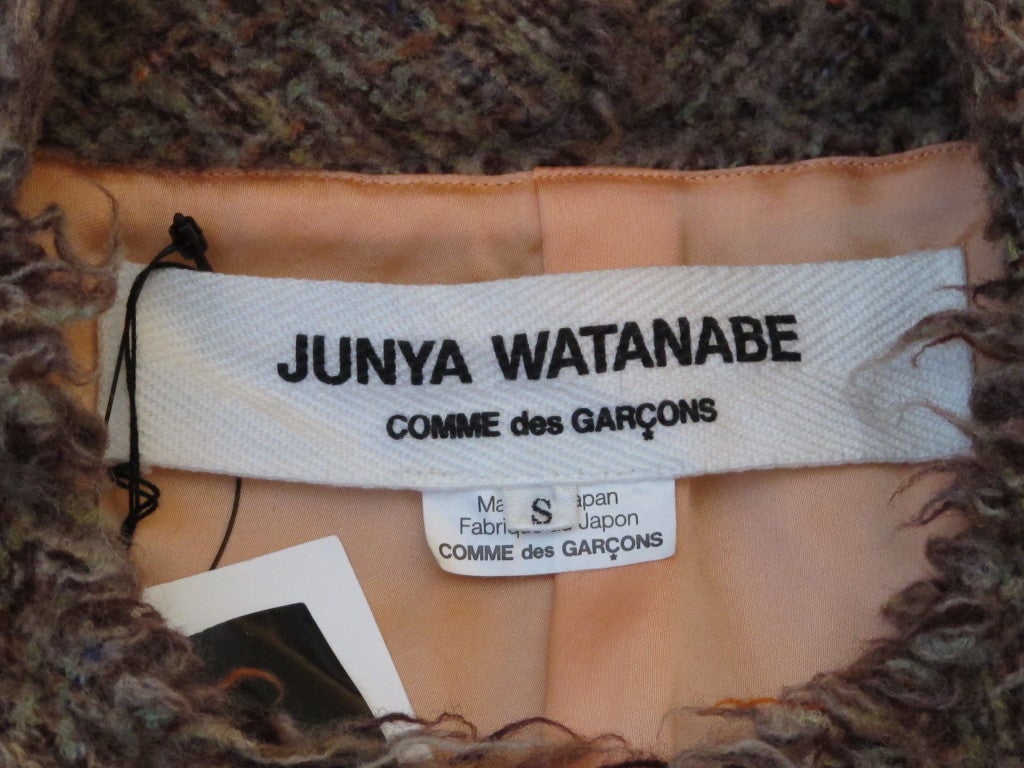 This is a Junya Watanabe for Comme des Garcons boucle wool jacket in shades of brown with orange thread accents that has never been worn - the tags are still attached. It is fully lined with a mellon-colored silky fabric called Cupra and comes with