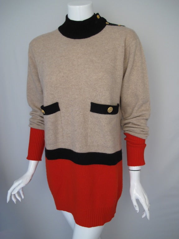A 1980s Chanel oversized 100% Scottish cashmere sweater in oatmeal, black and tomato red. Features clover buttons at the left side of the neck and on the front pockets an can be worn bloused or long. In very good to excellent condition with no