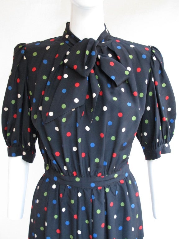 Vintage YSL 100% silk black with red, blue, green and white, polka dot day dress. Features two ties at the neck, slight shoulder pads with a full gathered short sleeve, drop pleats at the waist and invisible zipper sewn into the left side seam below