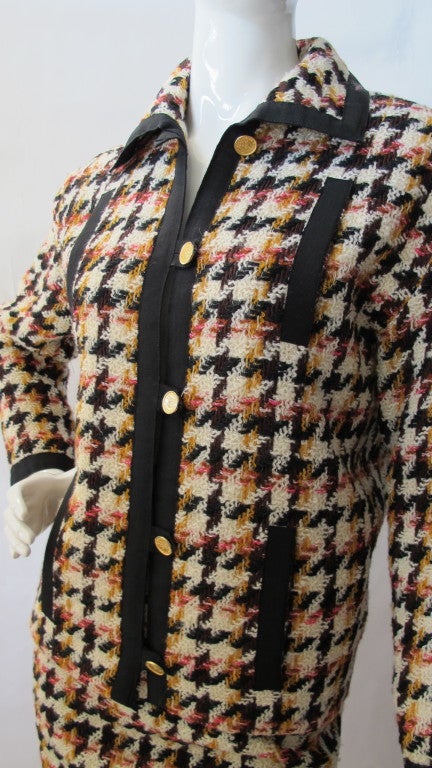 1980's Chanel boucle wool skirt and jacket suit in a houndstooth pattern of brown, black, yellow, off white and deep pink. The jacket is a box cut with a typical 80's drop shoulder and features four frontal black grosgrain slat pockets. Black