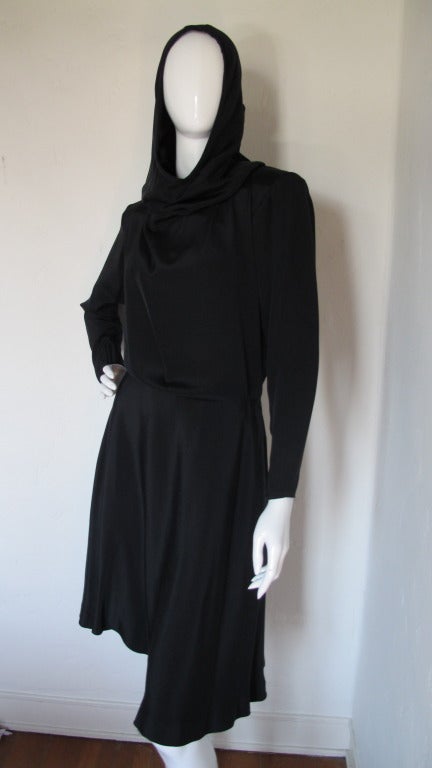 1990s Yves Saint Laurent dramatic black silk dress with hood that can be worn up or down. Features shoulder pads, sleeves that zipper at the cuff and closes by means of a zipper at the side of the skirt and snaps up the side of the blouse. Labeled