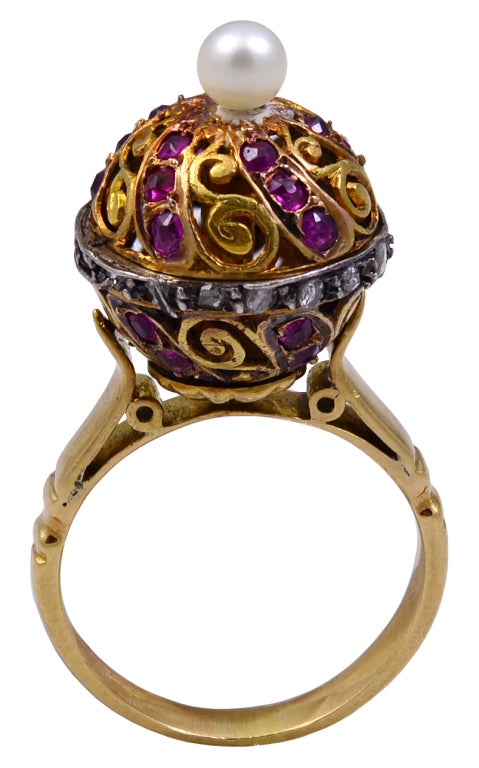 THE RING IS IN THE FORM OF A BALL AND SET WITH RUBIES AND WITH A ROSE DIAMOND COLLAR AND A PEARL FINIAL. THE COLLAR UNSCREWS TO OPEN THE BALL IN ORDER TO INSERT A PIECE OF SOLID PERFUME. THIS IS DONE IN ORDER TO AROUSE THE SENSES WHEN THE HAND IS