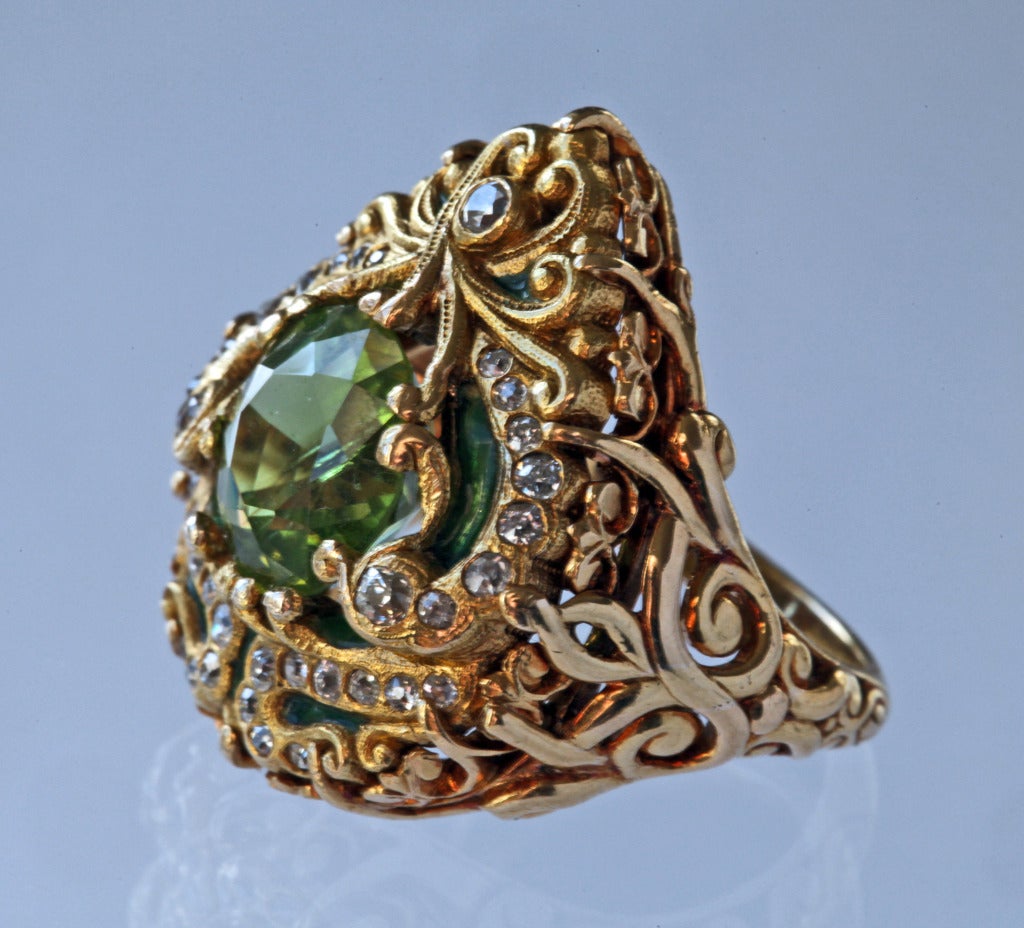 A superb enamelled gold & diamond Moghal Style ring by Marcus & Co in the form of a bejewelled Sultan's turban decorated with gold arabesques, 35 Victorian cut diamonds of approximately 0.45 carats & an exquisite peridot of approximately 4 carats. A