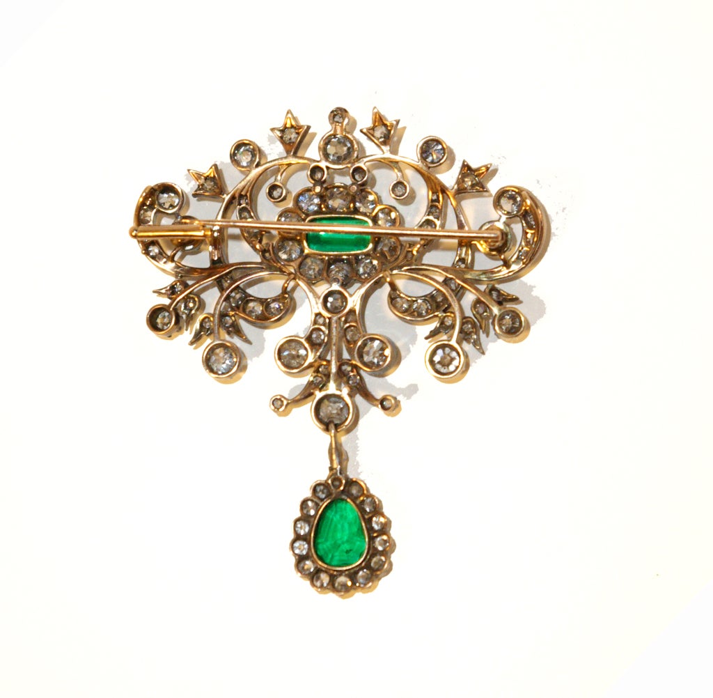 A lovely 19th century brooch/pendant of open work foliage design all set with brilliant cut diamonds (old European brilliant s) a central oval cluster of diamonds surrounding its original open backed emerald and diamond drop. Mounted in silver and
