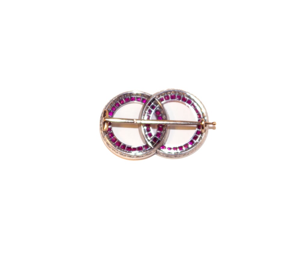 A fine quality brooch of the Art Deco period formed of 2 intertwined circles, each one set with small old mine cut diamonds and on the inside with matching bright calibre cut rubies. The platinum mount is finely millegrained and engraved,the brooch