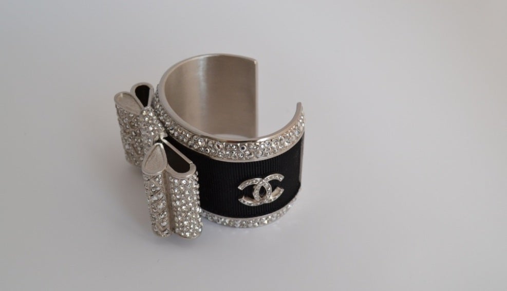 Cuff manchette Chanel 
Bow with Swarovski strass
CC symbols
Silver metal
Dimensions: 13.5 x 3.8 cms 
Never worn
It comes with velvet pouch

All ours items are 100% authentic and original. No fake or other awful imitations
We are French