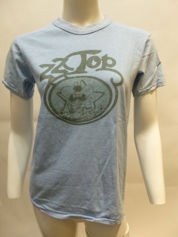 This is a T-shirt for ZZ Top, very early in their career. The double Z's have a very similar font to the Zs on the cover of the first LP from 1971, but I can't find this image or exact font anywhere. The tag definitely places this tee from early