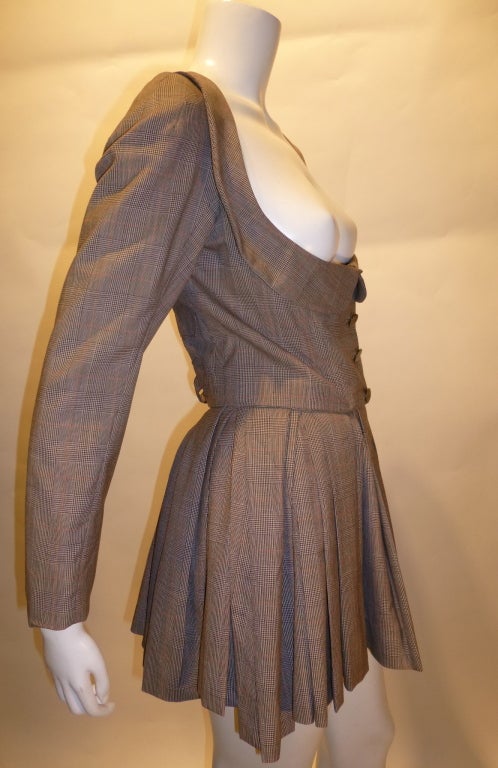 This is a two-piece glen plaid skirt suit with immodest bust from Dame Vivienne Westwood. This is from the Autumn/Winter 88/89 line. Logo buttons, full bust cut, buckles in the back and a very short, pleated circle skirt are among the beautiful