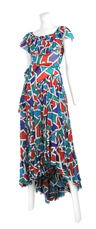 Soft cotton gown with vibrant geometric print. Classic YSL ruffle at hem and scoop neck. Sash belt at waist and side zip closure.
